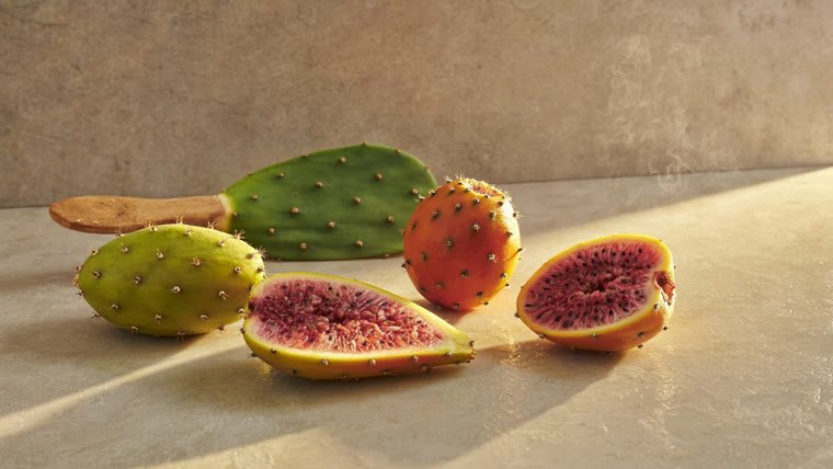 Figues de barbarie entières et une figue coupée montrant sa chair et ses graines, posées sur la pierre claire